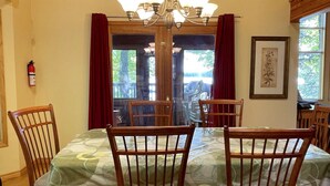 Un comedor con una mesa dispuesta para cuatro, sillas de madera, una araña, un extintor y un cuadro en la pared.