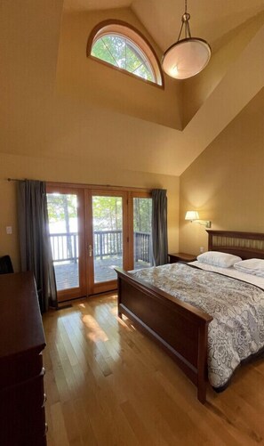 Quarto com uma cama grande, escrivaninha, janela com vista para o exterior e uma luminária no teto.