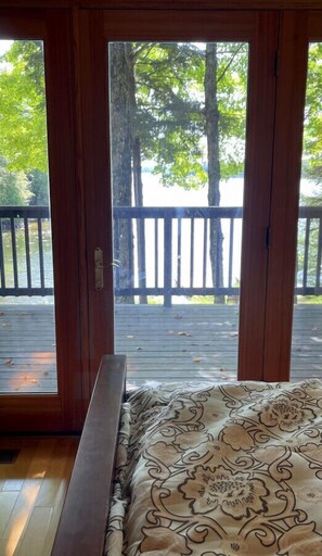 A room with a bed and a view through glass doors to a wooden deck with a railing.