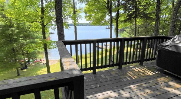 A wooden deck with a railing overlooking a lake, surrounded by trees.
