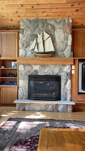 A stone fireplace with a ship model above it, wooden cabinets, and a patterned rug on the floor. - Chandos Lake Sanctuary (North Kawartha)