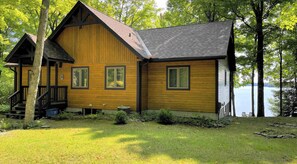 A cabin with a wooden exterior, a porch, and a view of a lake.