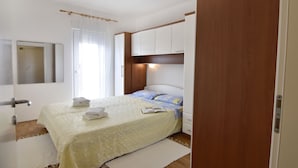 A bedroom with a bed, white curtains, a bedside table, a nightstand, and a wooden wardrobe. - Comfortable apartment near the beach Umag (Umag)