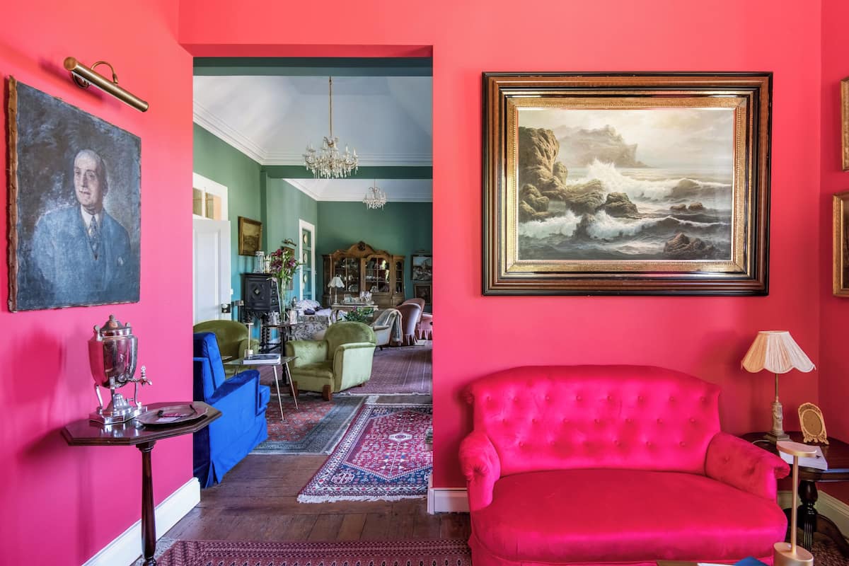 Ein Zimmer mit einem roten Sofa, einer Kristallleuchtre, einem Gemälde und einem Vintage-Radio.