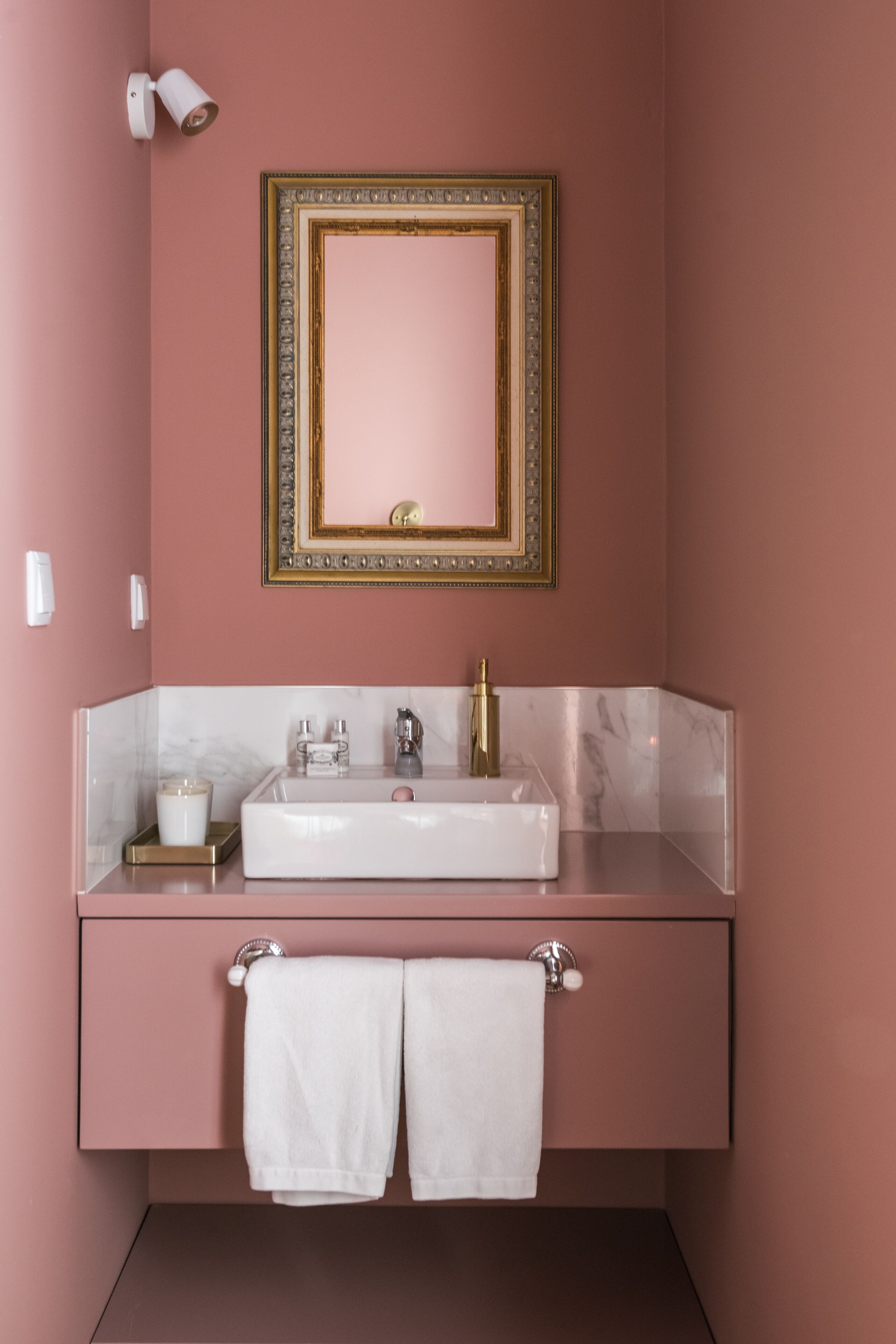 A bathroom with a white sink, gold faucet, and a mirror with a gold frame. There are two towels hanging from the sink area.