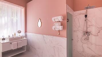 A modern bathroom with a pink wall, marble tiles, a white sink, and a shower.