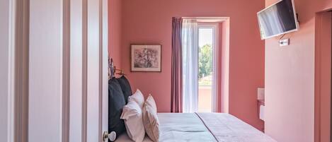 Un dormitorio con cama, televisor, un cuadro y ventana con cortinas.