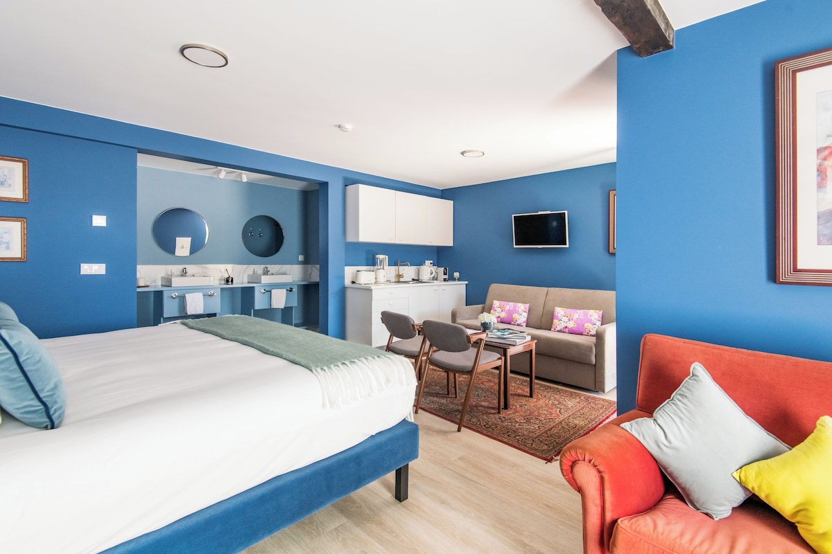 Ett modernt hotellrum med en säng, en soffa, en matplats och ett litet kök.