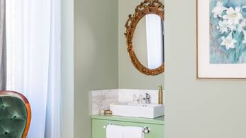 A bathroom with a green vanity, a white sink, a gold-framed mirror, and a framed floral painting on the wall.