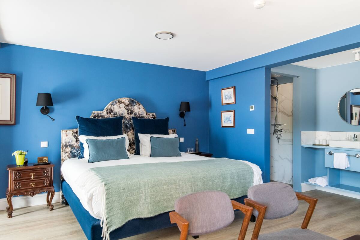 Ein Schlafzimmer mit einem großen Bett, zwei Nachttischlampen, einem Nachttisch, einem Sessel und einem Badezimmer mit Waschbecken und Spiegel.