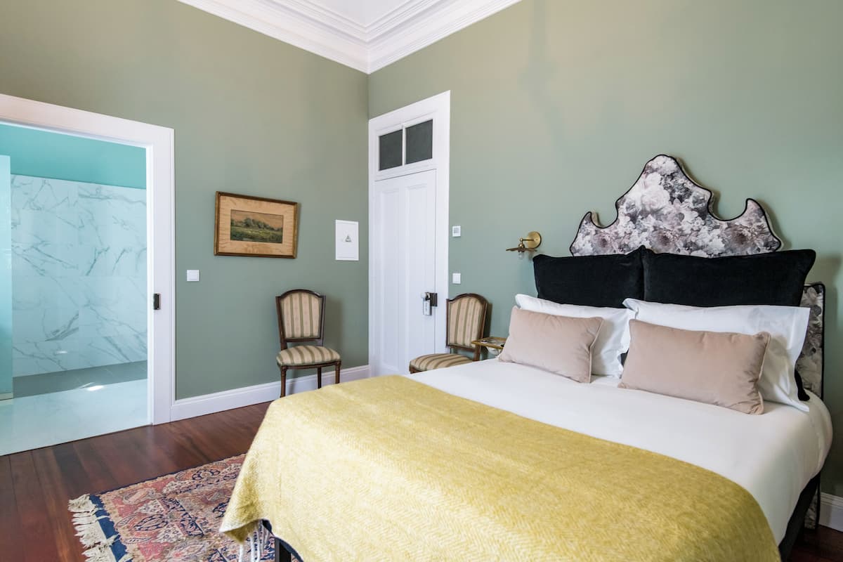Ein Schlafzimmer mit einem großen Bett, zwei Stühlen, einer Tür und einem Bild an der Wand.