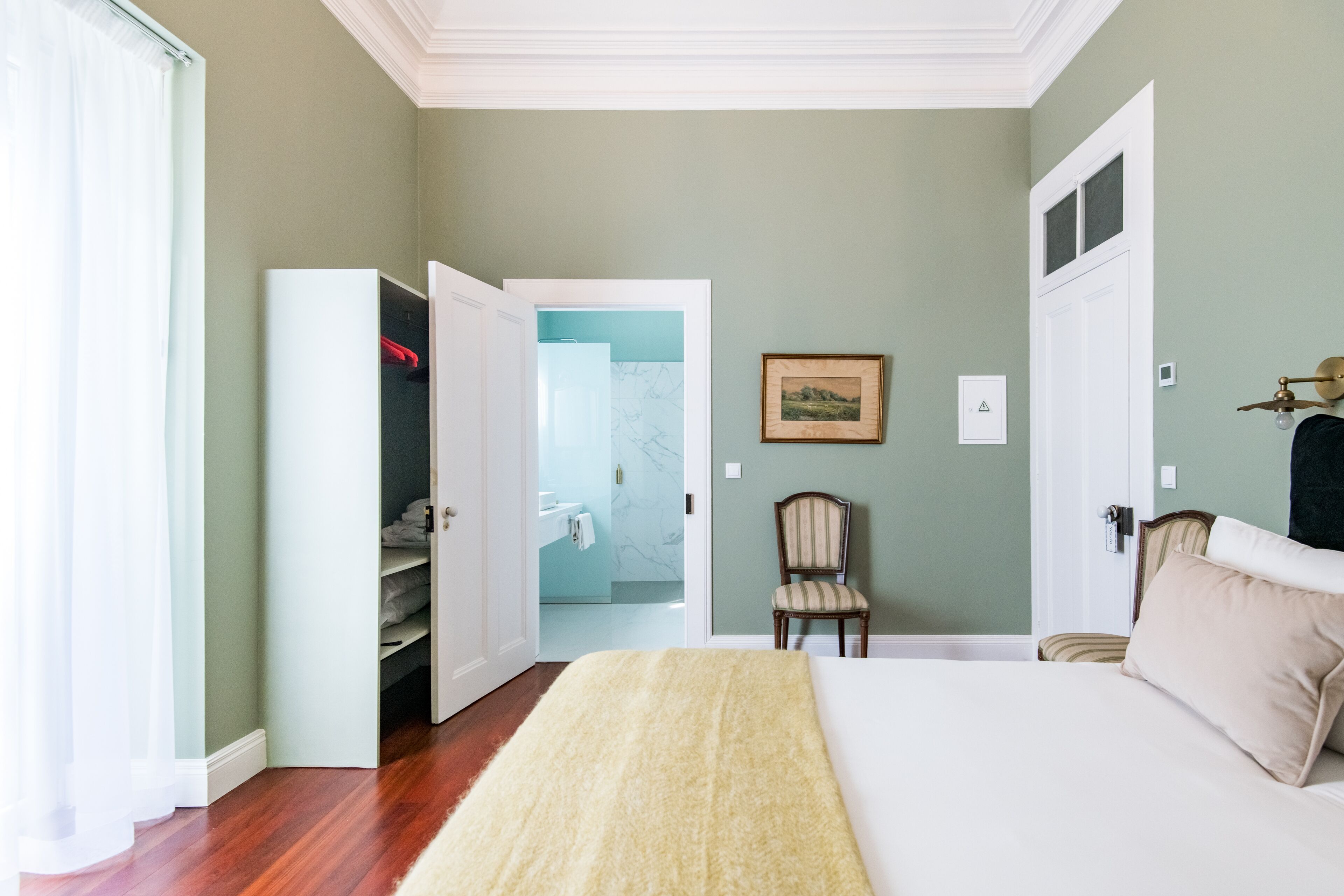 Un dormitorio con cama, una silla, un armario y una puerta que da a otra habitación.