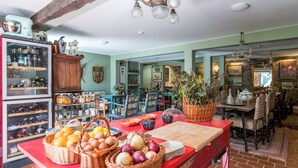 Une cuisine avec un îlot central rouge, des paniers en osier remplis de fruits et d’œufs, et un réfrigérateur à vin.