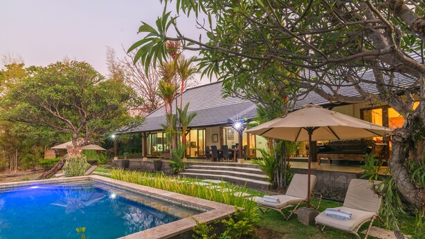 A poolside area with a swimming pool, lounge chairs, and a covered seating area with umbrellas. - Villa Lotus Kayuputih (Sukasada)