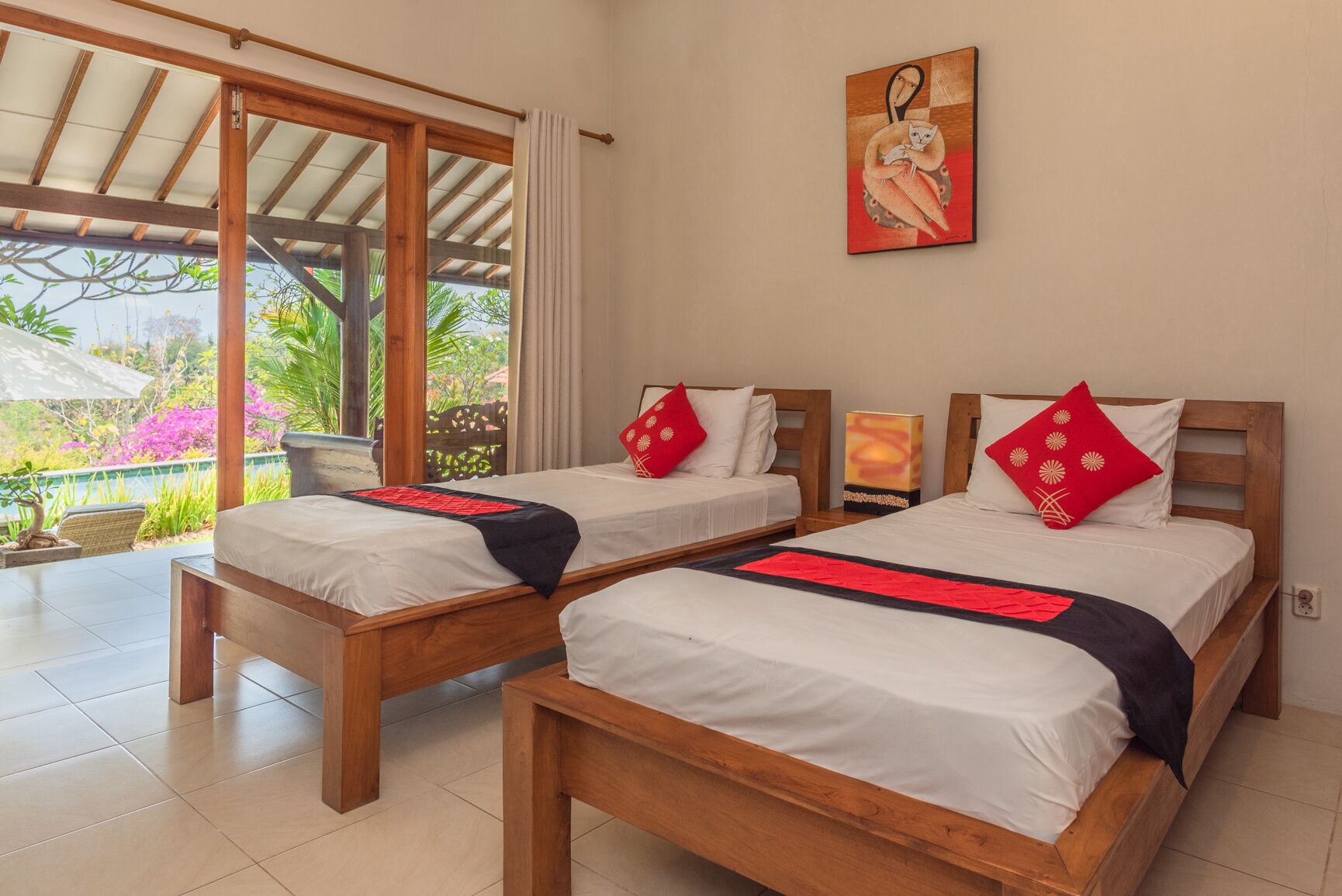 A hotel room with two wooden beds, a large window with a view of greenery, and a painting on the wall.