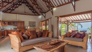 A spacious living area with wicker furniture, a wooden coffee table, and a view of the ocean. - Villa Lotus Kayuputih (Sukasada)