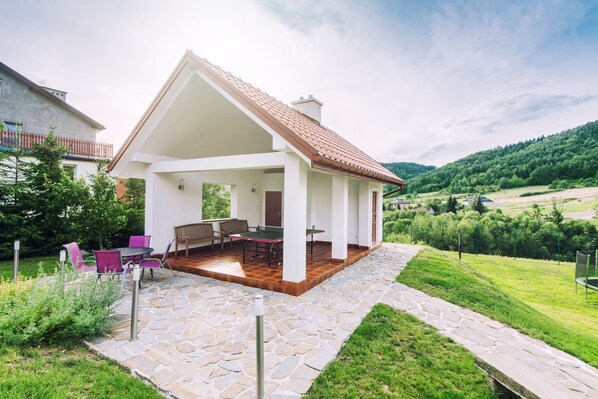 A house with a covered patio, stone flooring, and a view of a green landscape.