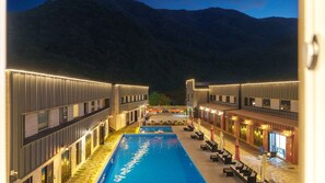 Un hôtel moderne doté d’une piscine centrale, d’un espace extérieur aménagé et offrant une vue sur les montagnes.