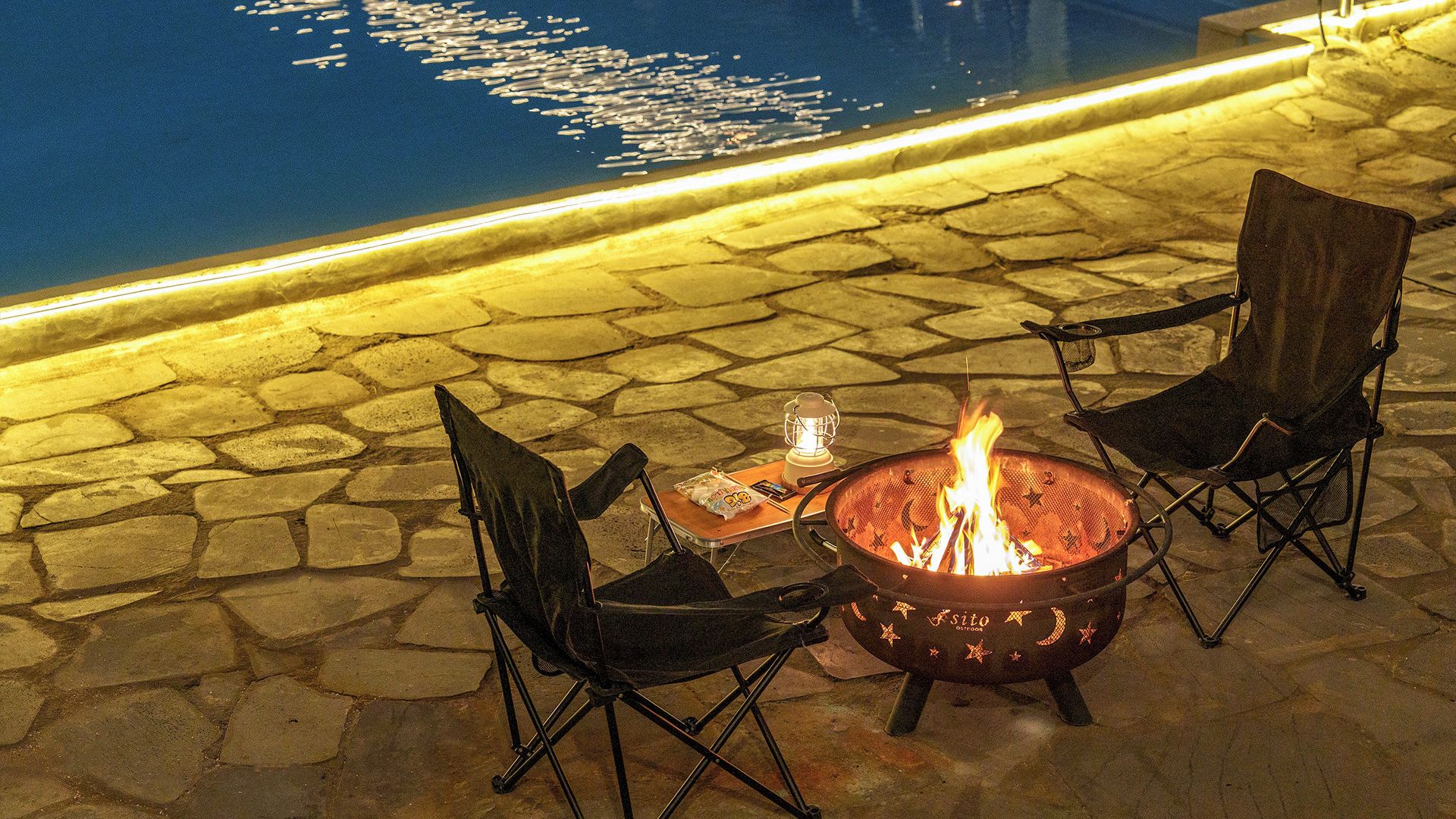 A fire pit with chairs and a table, surrounded by stone tiles.