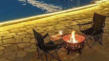 A fire pit with chairs and a table, surrounded by stone tiles.