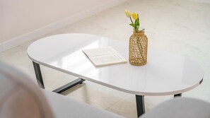 Een witte tafel met een boek en een rieten vaas met bloemen.