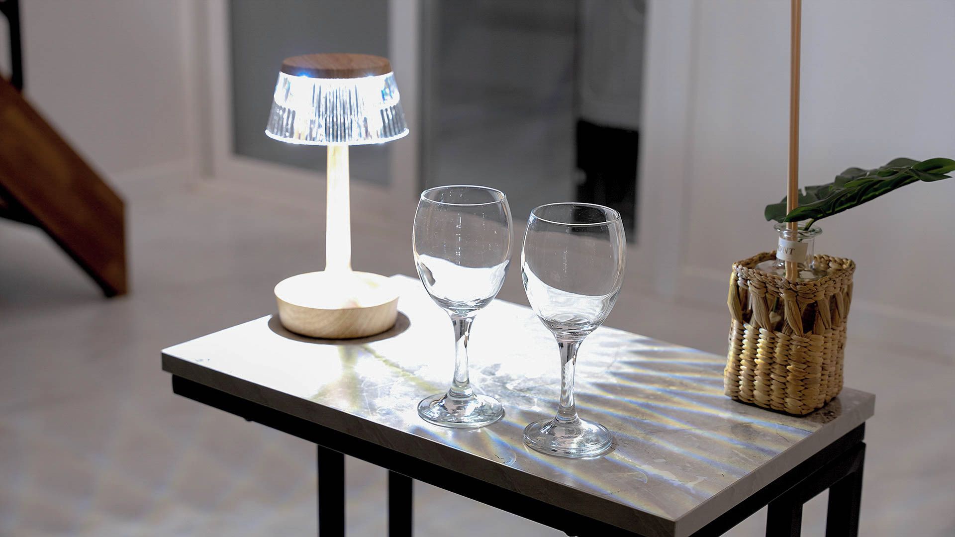 Une table avec deux verres transparents, une lampe et un panier en osier contenant une plante.