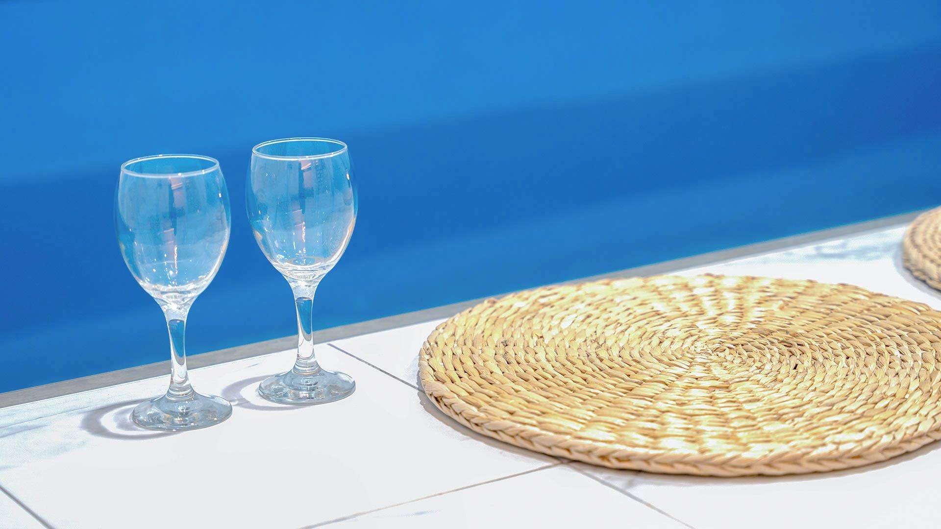 Dos vasos de vidrio transparentes sobre una superficie de azulejos blancos, con un tapete tejido cerca.