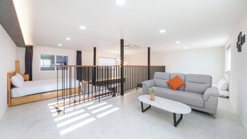 En moderne stue med sofa, seng, sofabord og trappe.
