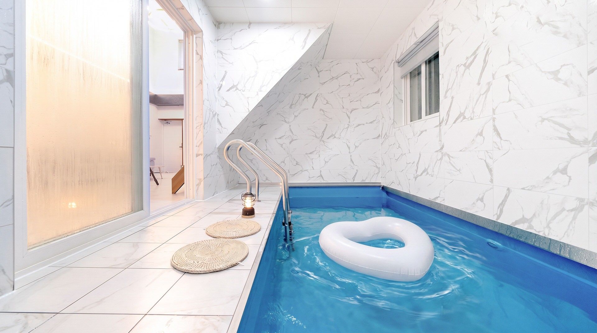 A modern indoor swimming pool with a clear blue water feature, a floating ring, and a built-in ladder.
