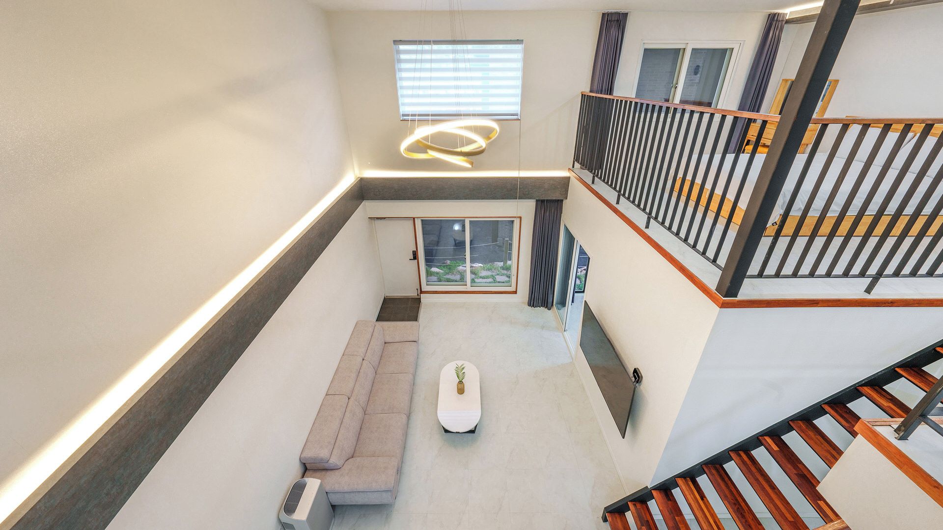 A modern interior with a central seating area, a staircase, and a view through a window.