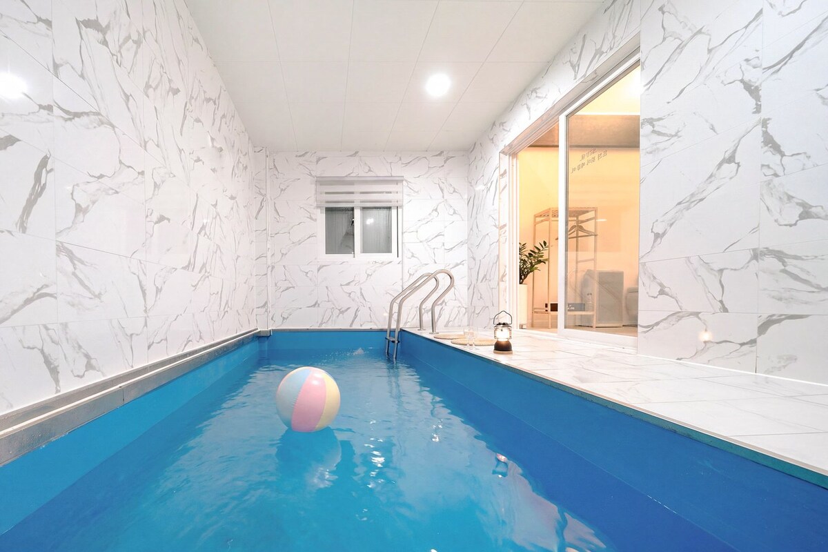 Une piscine intérieure aux murs de marbre, avec de l’eau bleue et un seul ballon.
