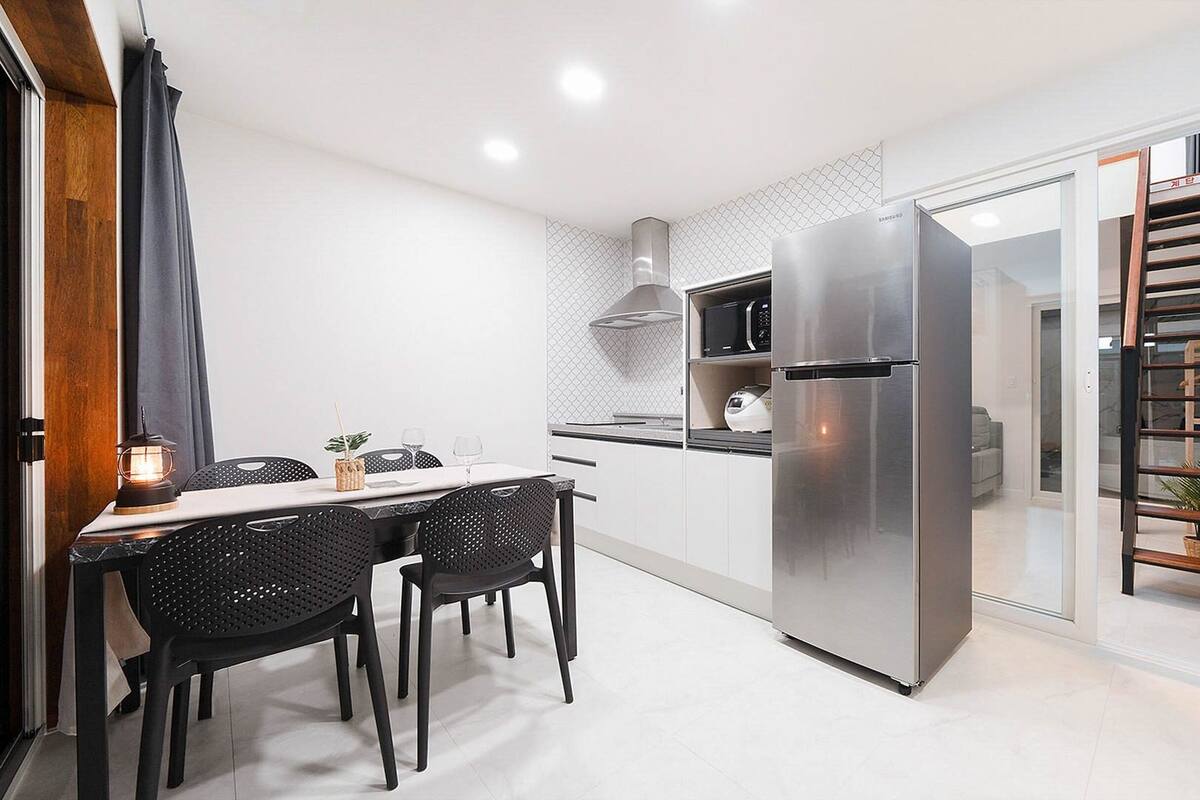 Une cuisine moderne équipée d’un réfrigérateur en acier inoxydable, d’un four à micro-ondes et d’un grille-pain. On y trouve une table à manger avec des chaises et une petite plante posée sur la table.