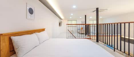 A bedroom with a wooden headboard, a bed with white bedding, a framed picture on the wall, and a staircase with a black railing.
