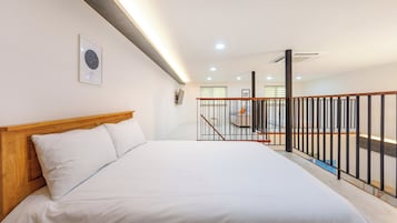 Un dormitorio con cabecera de madera, cama con ropa blanca, un cuadro en la pared y una escalera con barandilla negra.