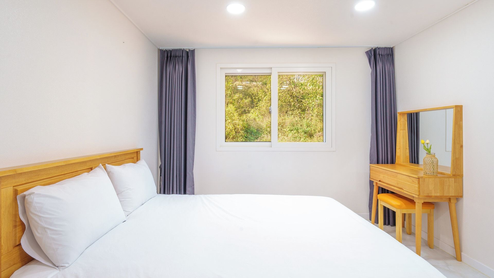 Un dormitorio con una cama, una ventana con cortinas, un tocador de madera y un espejo.