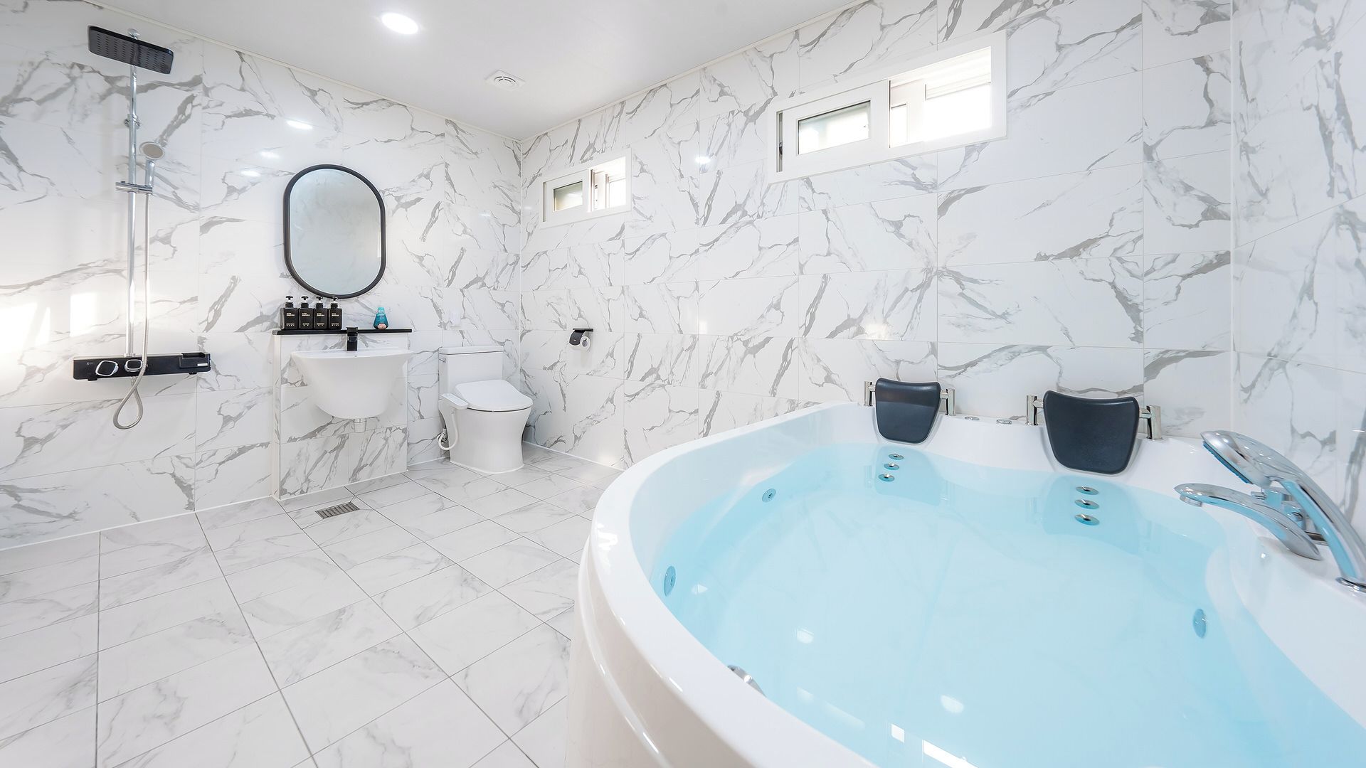 A modern bathroom with a marble wall, a freestanding bathtub, a toilet, and a shower.
