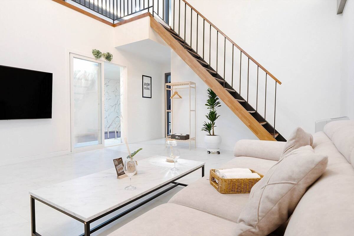 Un salon moderne avec un canapé, une table basse, un téléviseur, un escalier et une plante en pot.