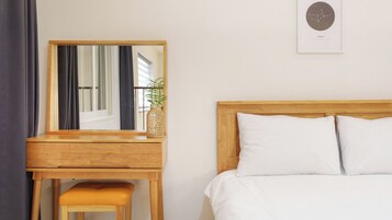 A bedroom with a wooden bed, white pillows, a wooden nightstand, a mirror, and a framed zodiac sign on the wall.