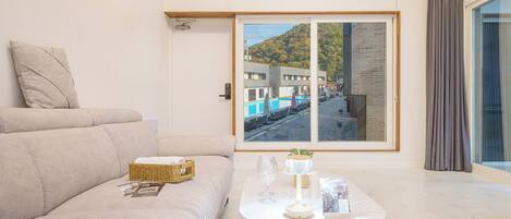 Una sala de estar moderna con un sofá, una mesa de centro con un florero de vidrio, una cesta de mimbre y un cuadro con una vista de un área de piscina.