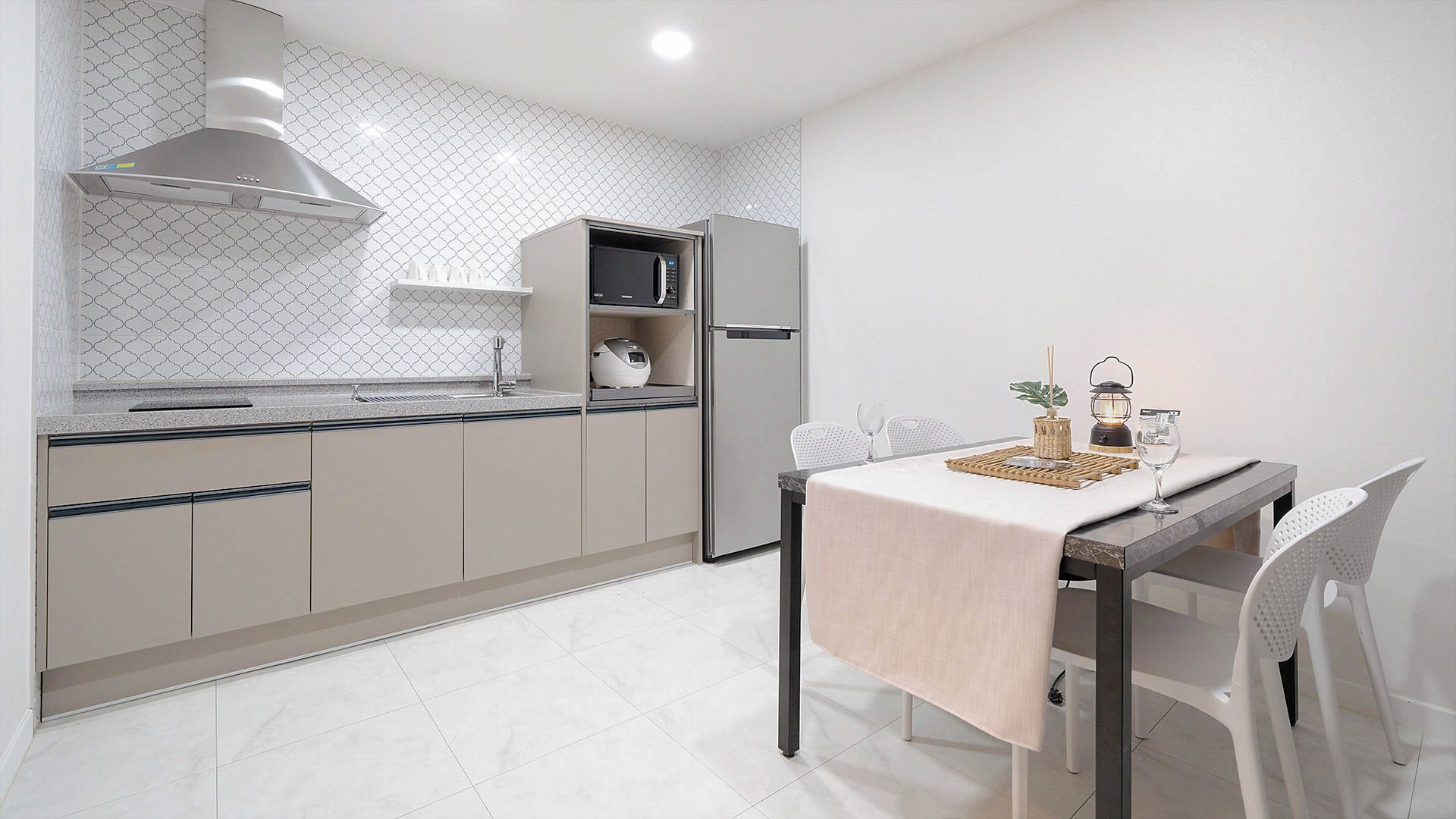 A modern kitchen with a dining area, featuring a stainless steel range hood, a microwave, and a refrigerator.