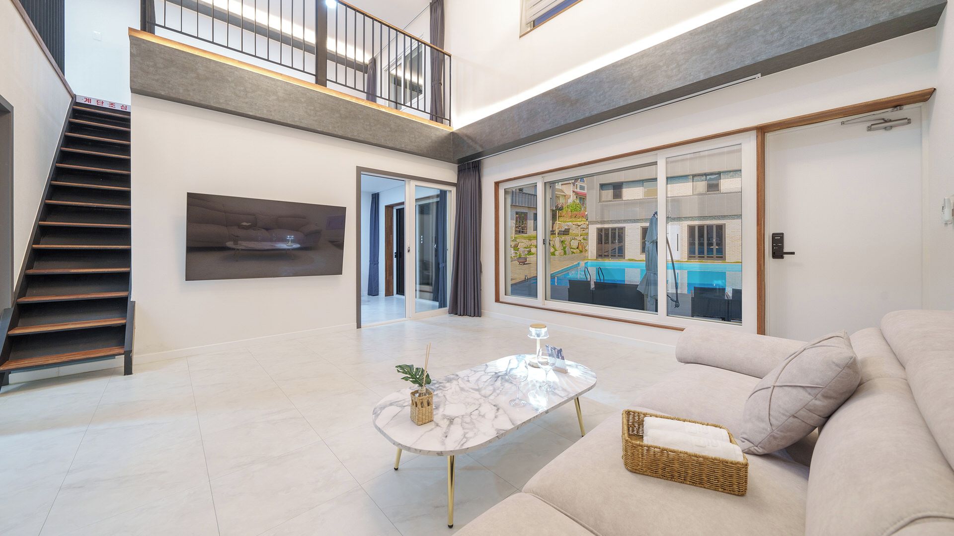 Amplia sala de estar con escalera, un ventanal con vista a una piscina y un sofá moderno.