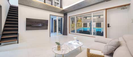 Amplia sala de estar con escalera, un ventanal con vista a una piscina y un sofá moderno.