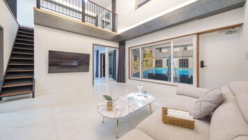 En rummelig opholdsstue med trappe, stort vindue med udsigt til et poolområde og en moderne sofa.