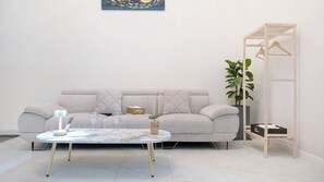 Een moderne woonkamer met een grijze bank, een ronde salontafel en een houten plantenstandaard.