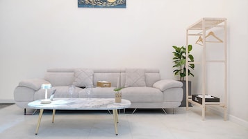Una sala de estar moderna con un sofá gris, una mesa de centro redonda y un atril de madera para plantas.