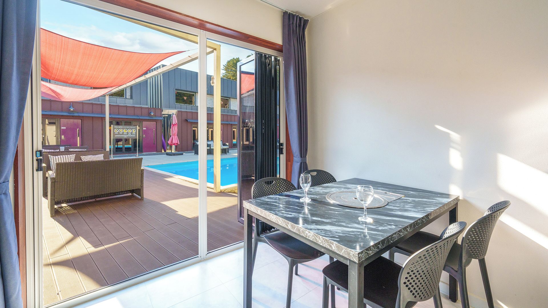 Una habitación con puerta de vidrio que da a una zona de piscina, una mesa de comedor con sillas y vista a la piscina.