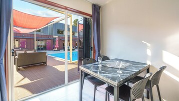 A room with a glass door leading to a pool area, a dining table with chairs, and a view of the pool.