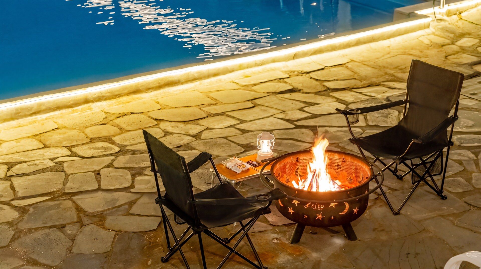 A stone patio with a fire pit and two chairs.