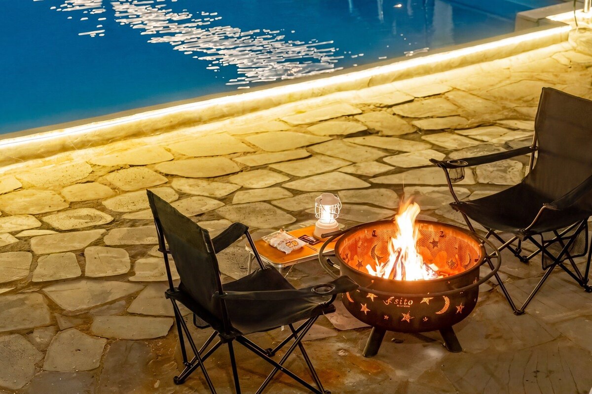 Une terrasse en pierre avec un foyer et deux chaises.