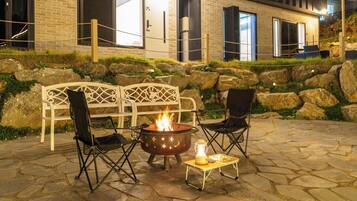 An outdoor seating area with a fire pit, two chairs, and a table with a lantern.